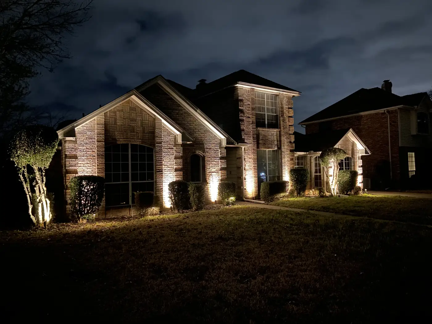 Warm light washing the brick gables and trees of a DFW home at night